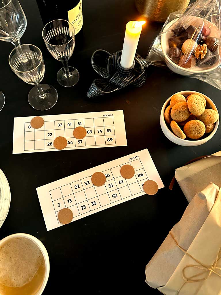 The image depicts a cozy and festive bingo event setup with Christmas-themed decorations. The room features a table with a grid of bingo cards, each card having a Christmas-related theme, such as 'Santa's List' and 'Holiday Wishes'.