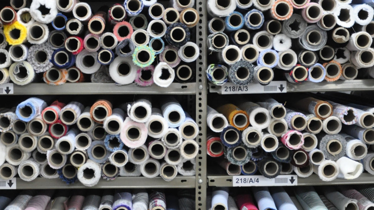 Multiple spools of fabric in various colors stacked on shelves.